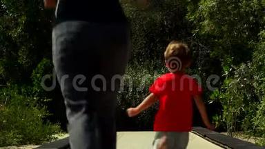 有趣的小男孩和妈妈一起在公园的蹦床跑道上奔跑和跳跃。